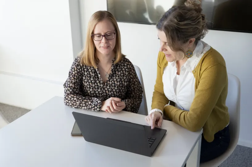 Kaksi naista keskustelee kannettavan tietokoneen äärellä toimistossa.
