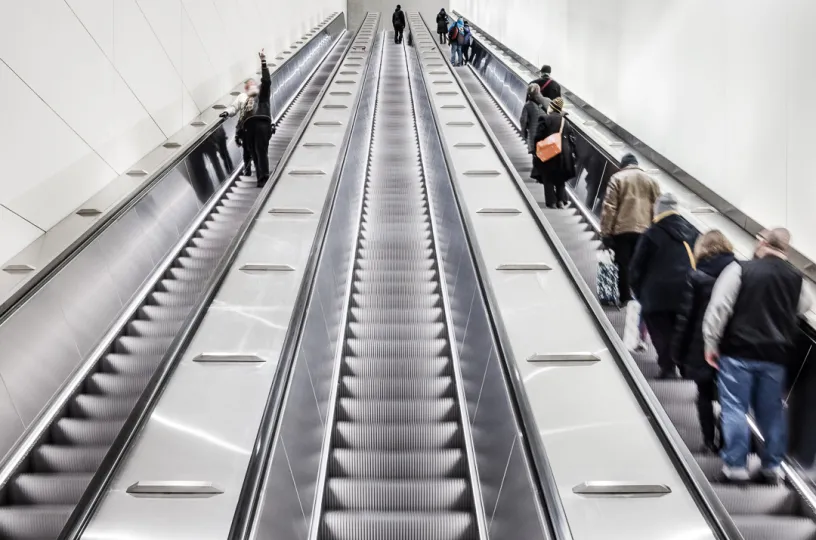 Pitkät liukuportaat metroasemalla, ihmisiä nousee ja laskee.