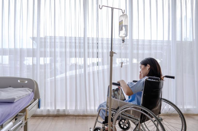 nuori nainen istuu pyörätuolissa sairaalassa ja katselee tablettia
