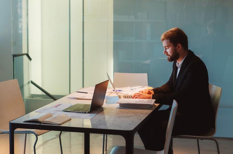 Mies istuu yksin toimistossa ja katsoo kannettavaa tietokonetta.