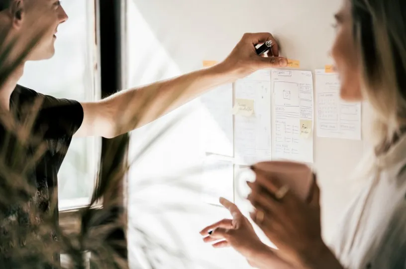 Kaksi henkilöä suunnittelee muistiinpanolappujen äärellä, toinen pitelee kuppia.