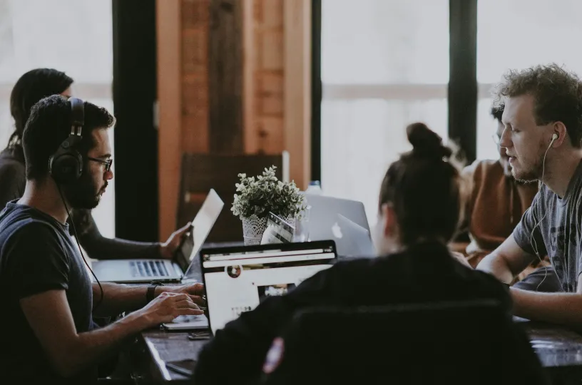 Neljä henkilöä työskentelee yhdessä pöydän ääressä kannettavien tietokoneiden kanssa.