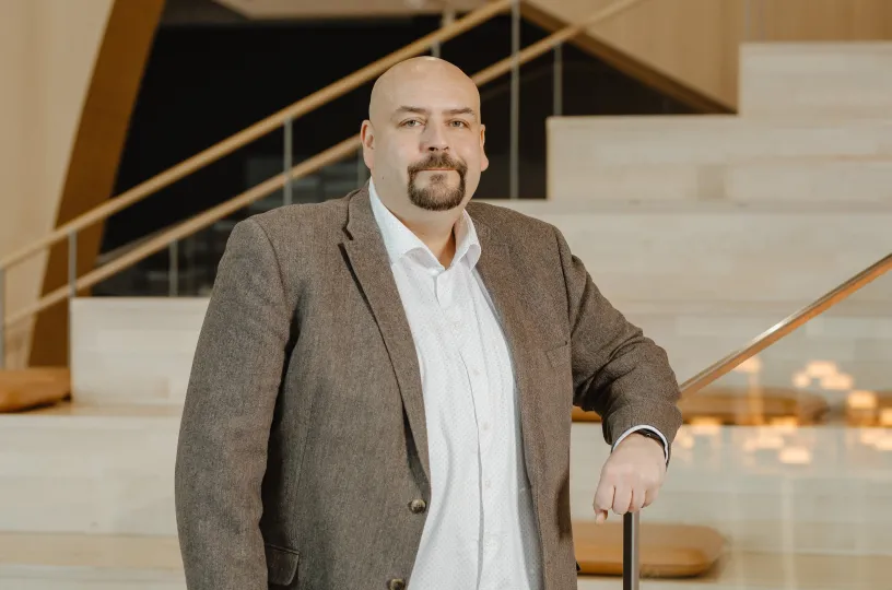 Henrik Haapajärvi seisoo portaikon edessä ruskeassa puvuntakissa ja valkoisessa paidassa.