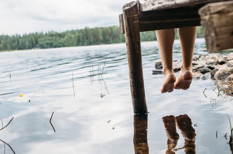 nainen istuu laiturilla järven rannalla