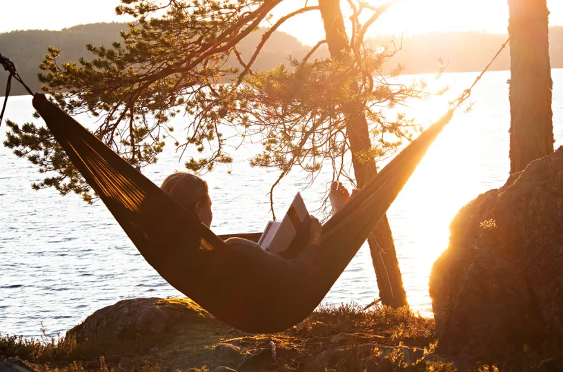 nainen lukee kirjaa riippumatossa auringonlaskun valossa