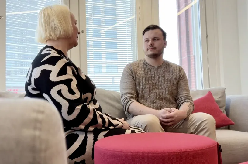 Kaksi henkilöä keskustelee sohvalla valoisassa toimistossa.