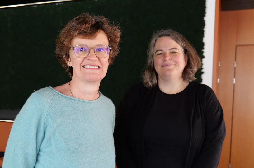 Kaksi hymyilevää naista seisoo vierekkäin sisätiloissa.