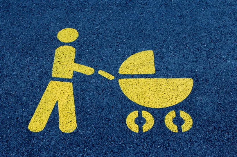 Vaakakuva tummaan asfalttiin keltaisella maalatusta tieliikennemerkinnästä, jossa henkilö työntää lastenvaunuja. 