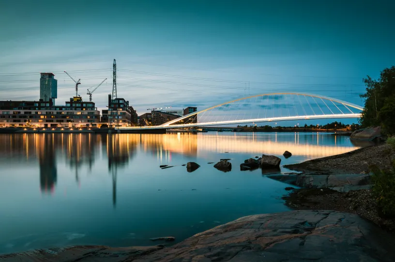 Vaakakuva, jossa maisema Mustikkamaalta Kalasatamaan. Kuvassa valkoinen riippusilta, nostureita ja tornitaloja. 