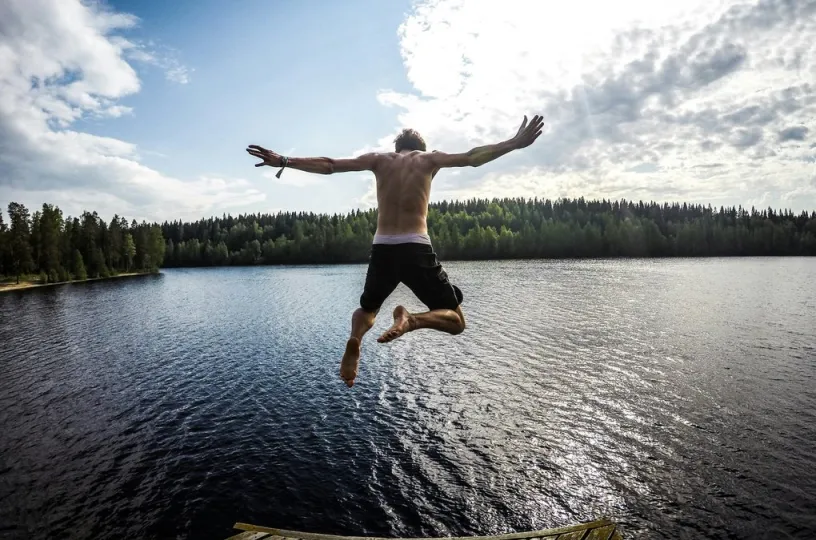 Henkilö hyppää laiturilta järveen aurinkoisena päivänä.
