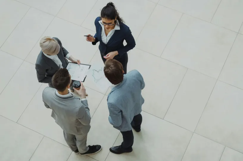 Neljä ihmistä keskustelee virastossa, katsottuna ylhäältä päin.