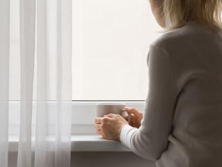 Nainen katsoo ikkunasta pidellen kahvikuppia