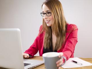 Hymyilevä nainen työskentelee tietokoneella.