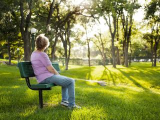 nainen istuu puistonpenkillä selin kameraan 