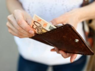 Nainen laittaa seteleitä lompakkoon, raha ja talous