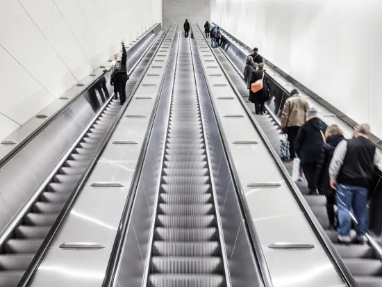 Pitkät liukuportaat metroasemalla, ihmisiä nousee ja laskee.