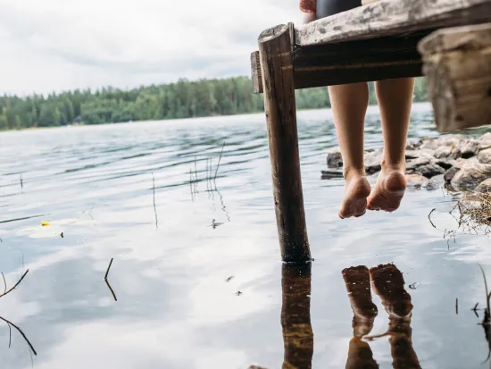 nainen istuu laiturilla järven rannalla