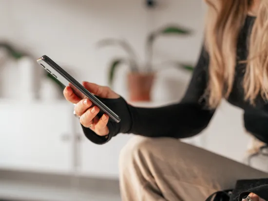 Henkilö pitää älypuhelinta kädessään sisätiloissa, taustalla kasveja.