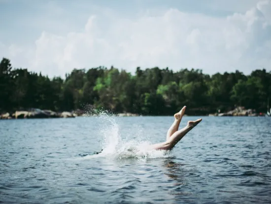 Ihminen hyppää veteen järvessä, vain jalat näkyvät pinnan yllä.
