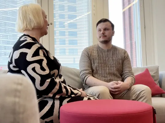 Kaksi henkilöä keskustelee sohvalla valoisassa toimistossa.