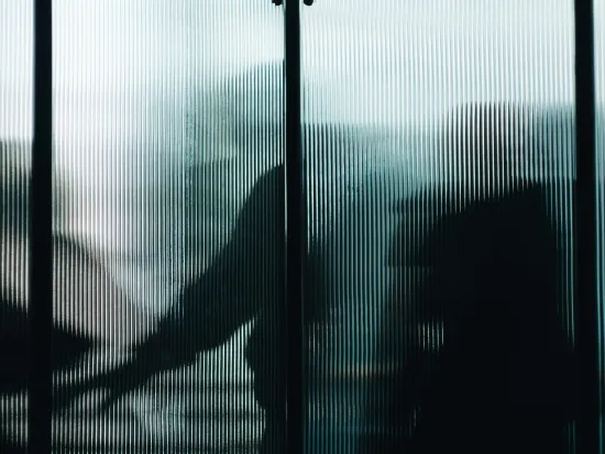 Sumeat hahmot lasiseinän takana, taustalla hämyistä valoa.