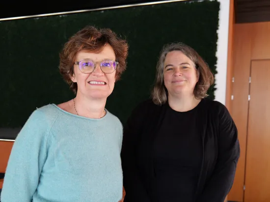 Kaksi hymyilevää naista seisoo vierekkäin sisätiloissa.