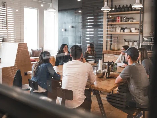 Seitsemän ihmistä keskustelee pöydän ääressä modernissa toimistossa.