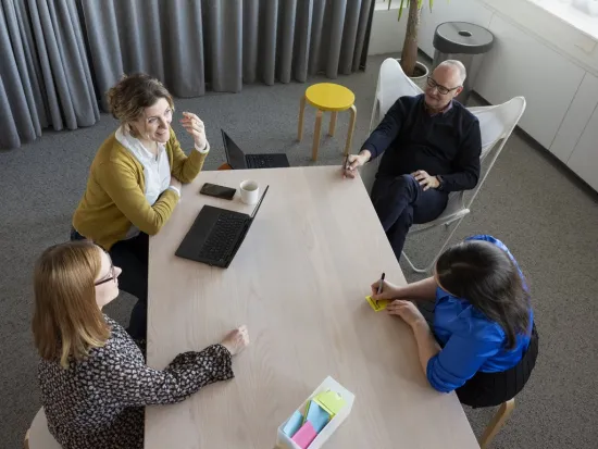 Neljä henkilöä neuvottelee toimistopöydän äärellä.