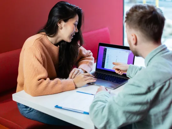 Kaksi henkilöä työskentelee yhdessä tietokoneella pöydän ääressä.