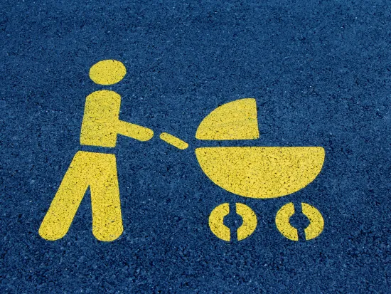 Vaakakuva tummaan asfalttiin keltaisella maalatusta tieliikennemerkinnästä, jossa henkilö työntää lastenvaunuja. 