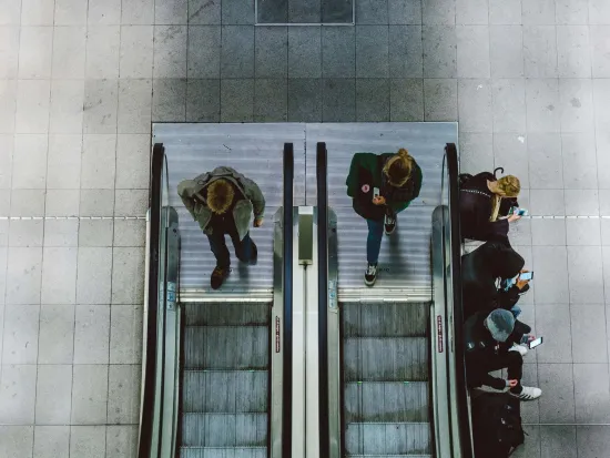 Kuvassa ihmisiä työmatkalla nousemassa rullaportaisiin.