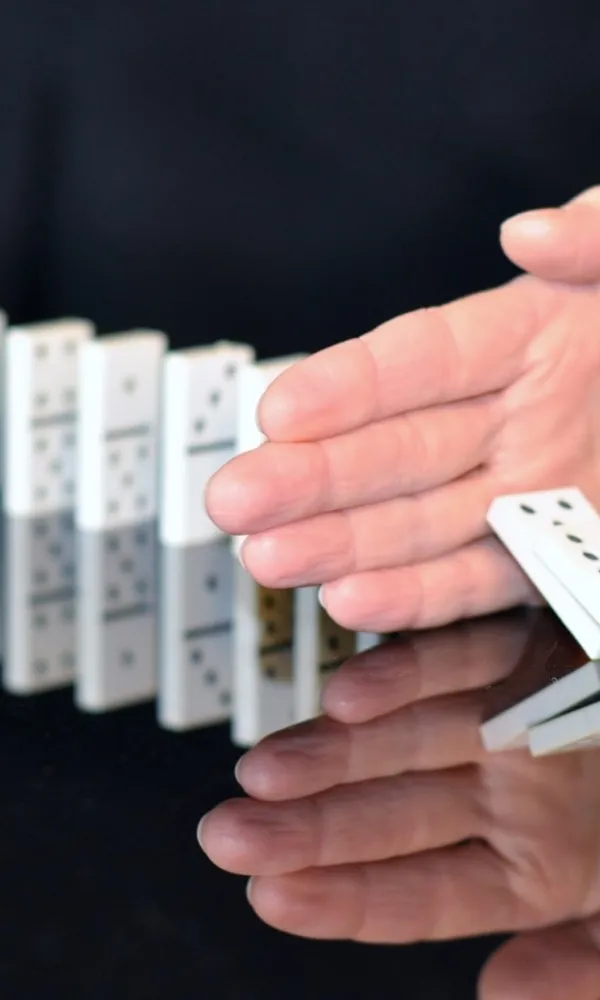 Käsi pysäyttää kaatuvat dominopalikat pöydällä.
