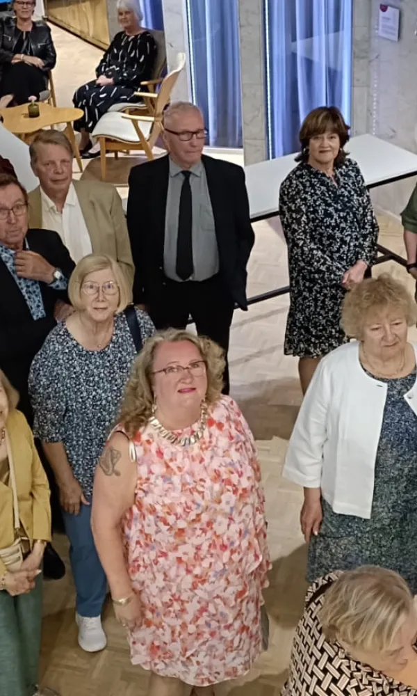Pro seniorit seisoo sisätiloissa, monet katsovat ylöspäin kameraan.