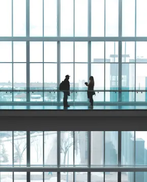 Kaksi ihmistä keskustelee lasiseinäisellä käytävällä.