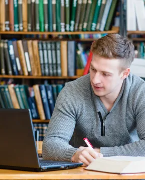 mies istuu pöydän ääressä ja katsoo avoinna olevaa kannettavaa tietokonetta